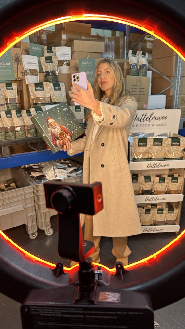 Derya filmt sich mit dem Smartphone im Lager von Dattelmann und hält einen Dattelmann-Adventskalender, im Vordergrund ein Ringlicht